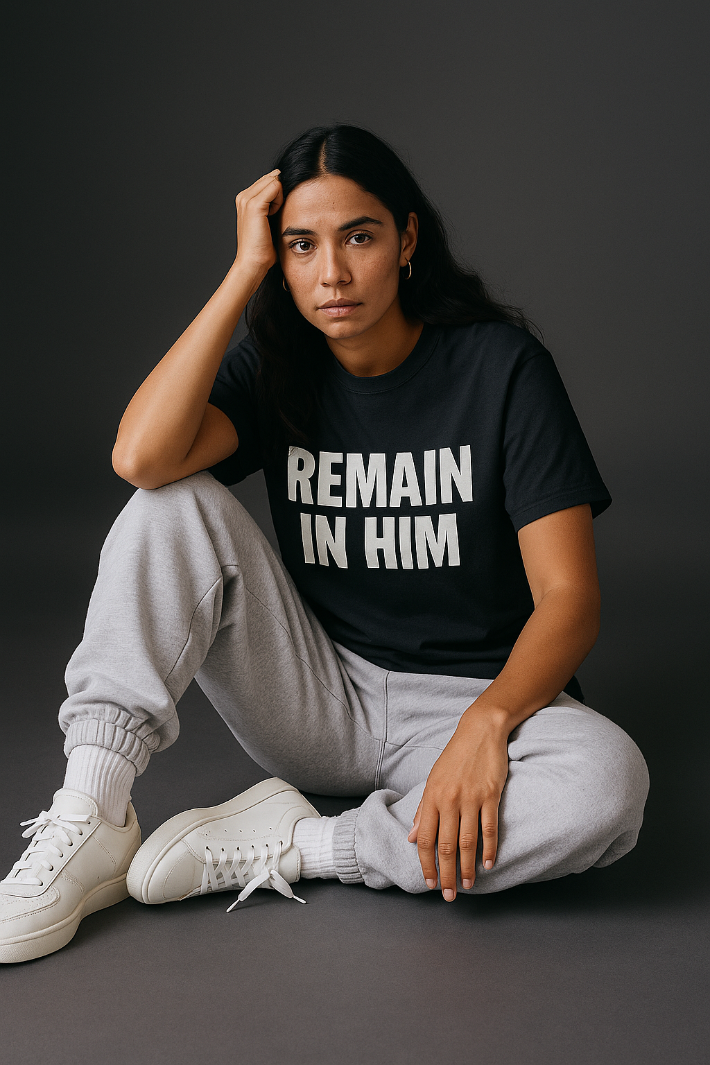 Person wearing a black t-shirt with 'REMAIN IN HIM' text, sitting on a dark background