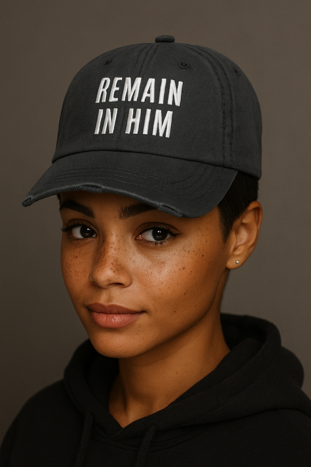a woman wearing a black cap with 'REMAIN IN HIM' text against a brown background