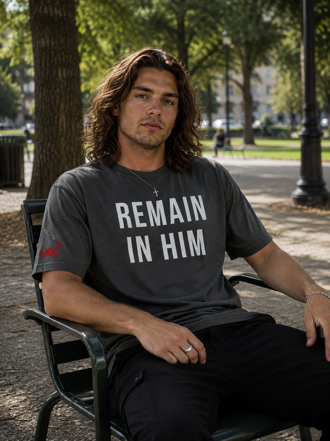 Man sitting outdoors wearing a t-shirt with 'REMAIN IN HIM' text