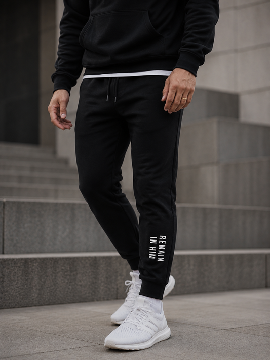 Person wearing black jogger pants with text and white sneakers on a concrete surface.
