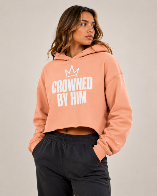 Woman wearing a peach hoodie with 'Crowned by Him' text on a plain background