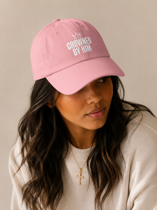 Person wearing a pink cap with 'Crowned by Him' text on a neutral background