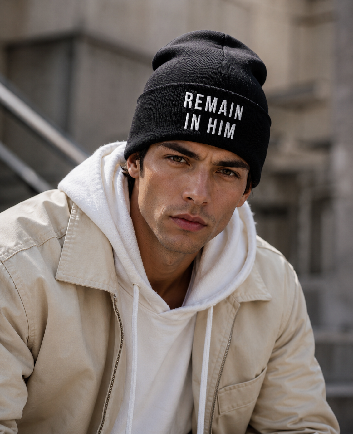 Man wearing a black beanie with 'REMAIN IN HIM' text, sitting outdoors.